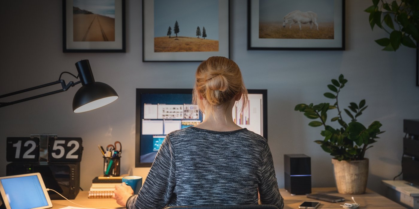 Mujer de espaldas trabajando en su casa de forma remota uando un monitor en un escritorio