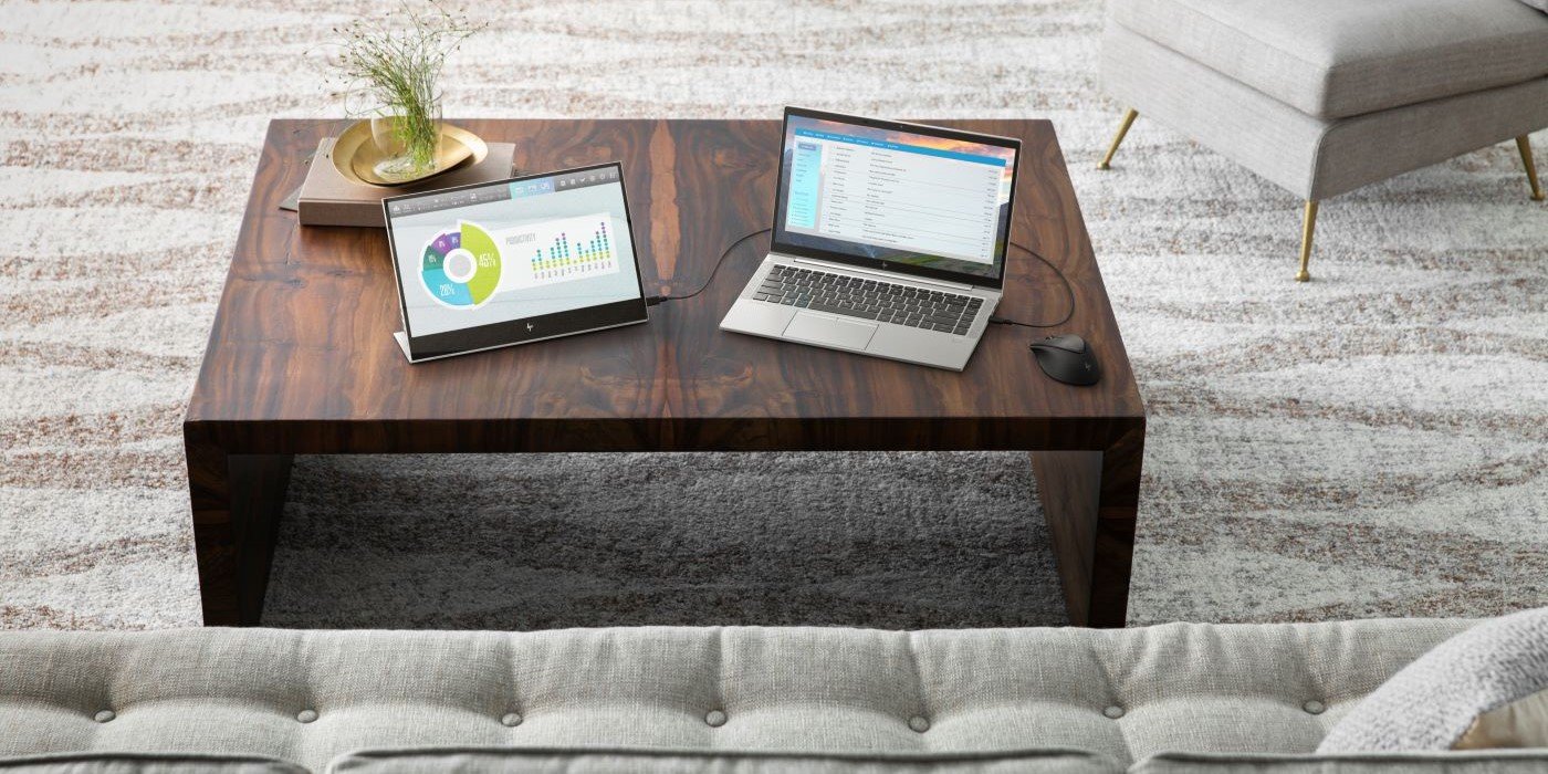 Laptop HP y monitor portátil conectados sobre mesa de madera en sala de estar moderna